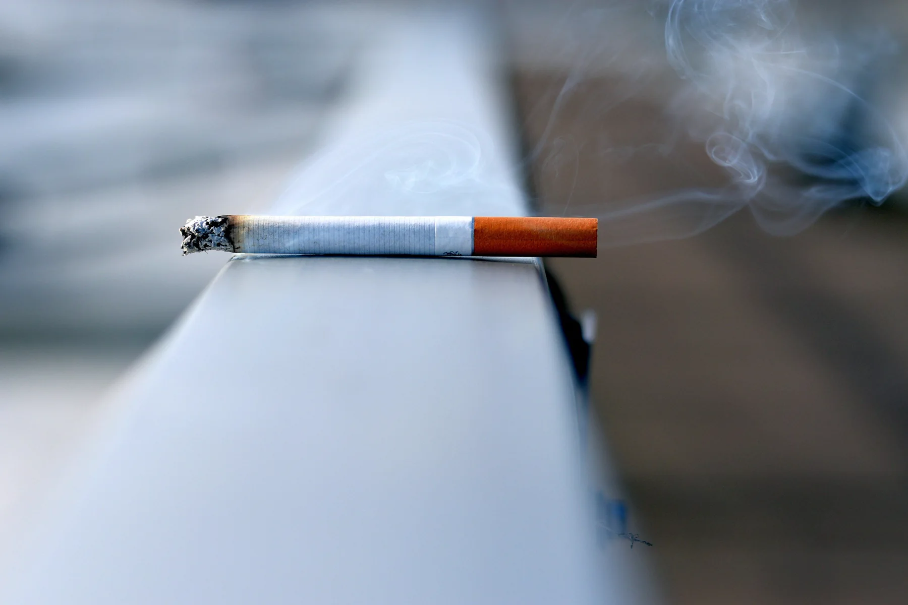 A lit cigarette resting on the edge of a desk, smoke drifting up