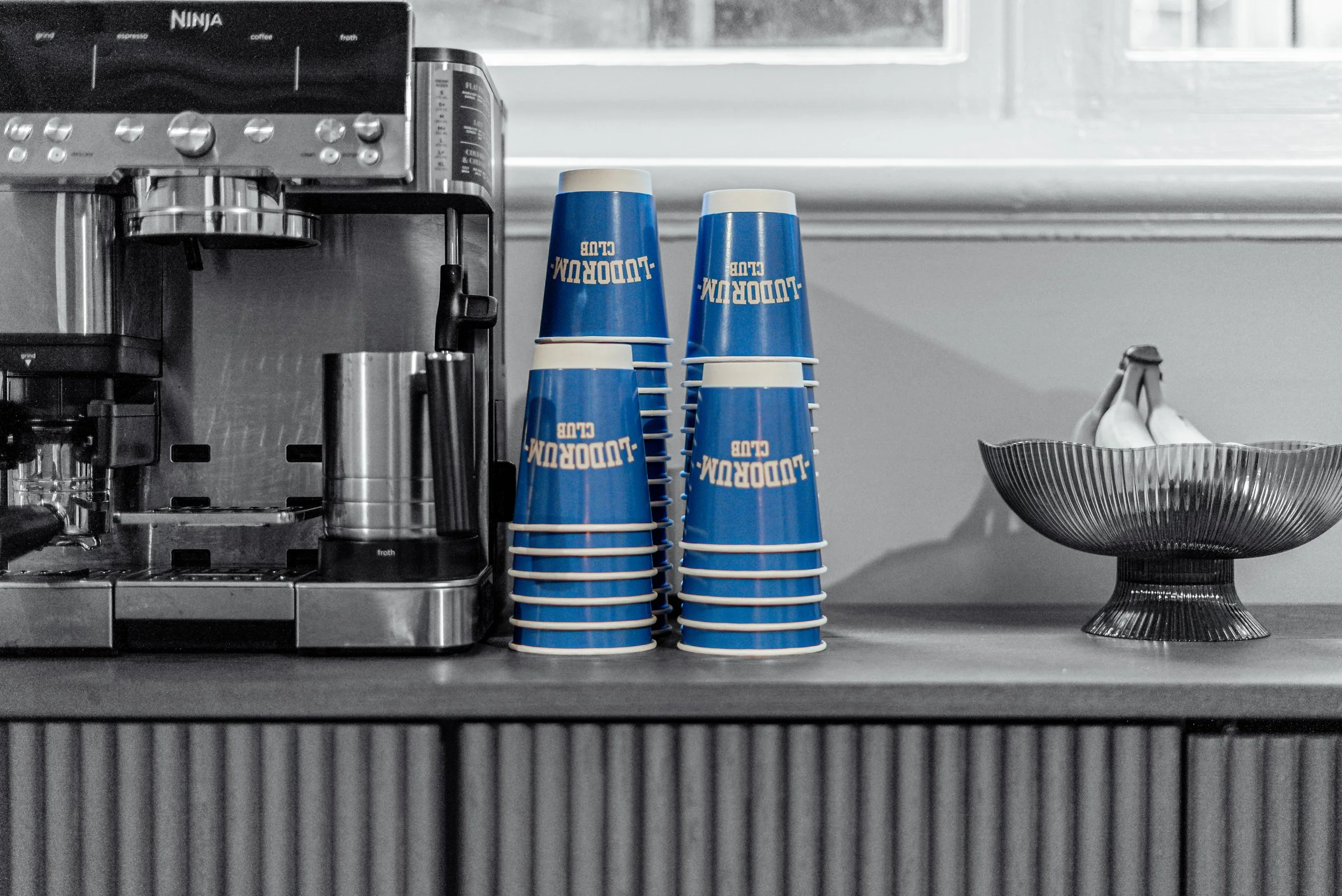 Blue Ludorum Club coffee cups stacked by the espresso machine