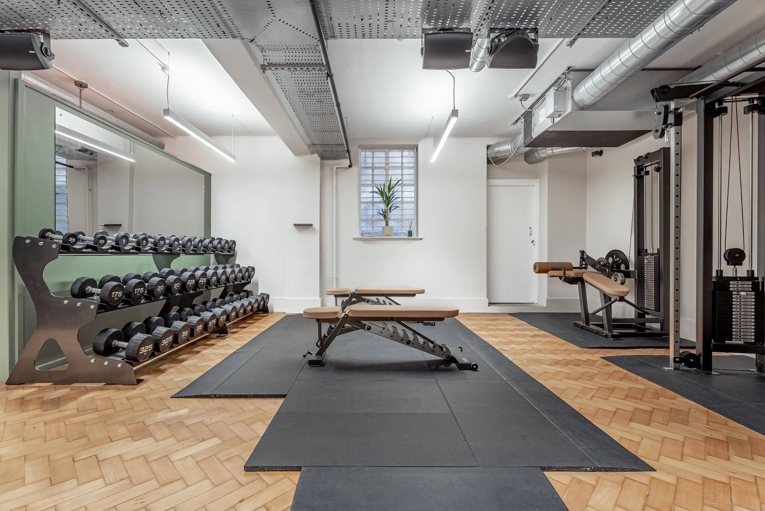 The gymnasium: dumbbell rack, two adjustable benches on rubber matting, cable machine, parquet floor
