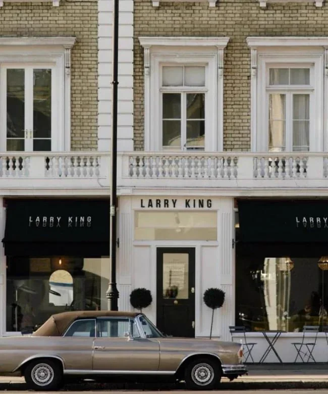 The Larry King salon front, black awnings on a white stucco building, with a vintage car parked outside