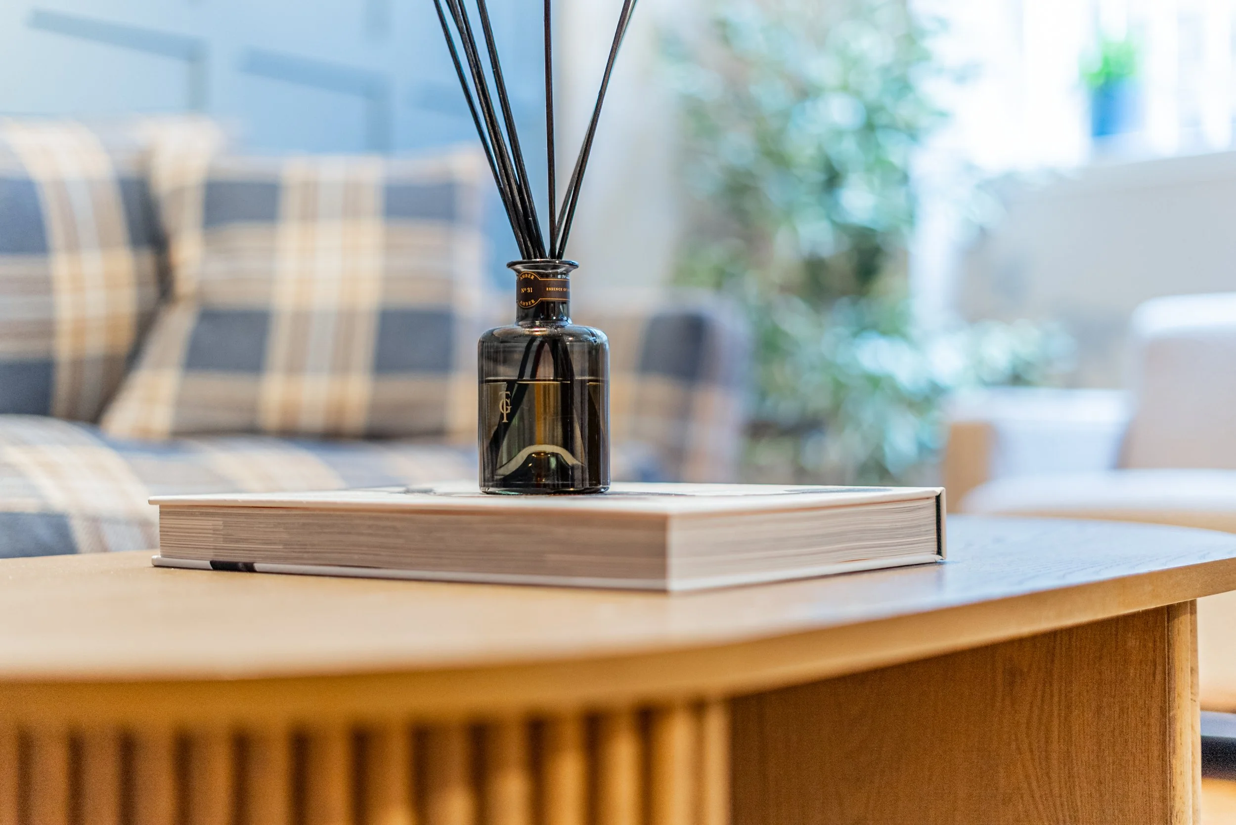 A reed diffuser on a book on the lounge table, tartan cushions behind