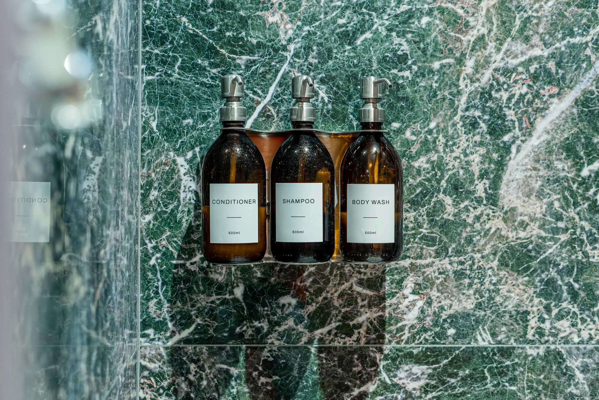 Amber glass bottles of conditioner, shampoo and body wash mounted on green marble